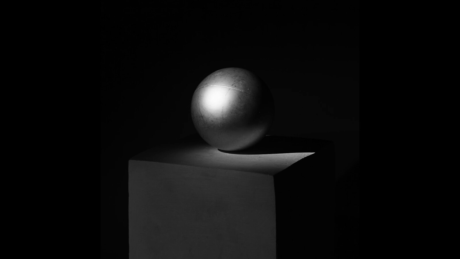 A sphere and geometric plinth illuminated by dramatic low-key studio light